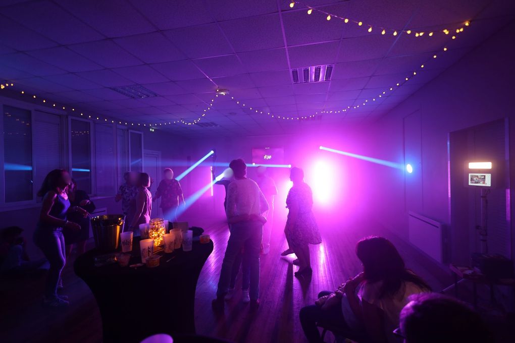 Piste de danse éclairée en violet lors d'une réception de mariage avec des invités, des guirlandes lumineuses et une cabine de DJ.