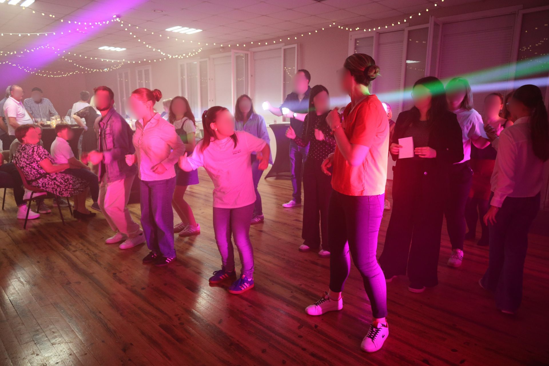 Des gens dansent dans une salle faiblement éclairée par des lumières de fête roses et vertes.