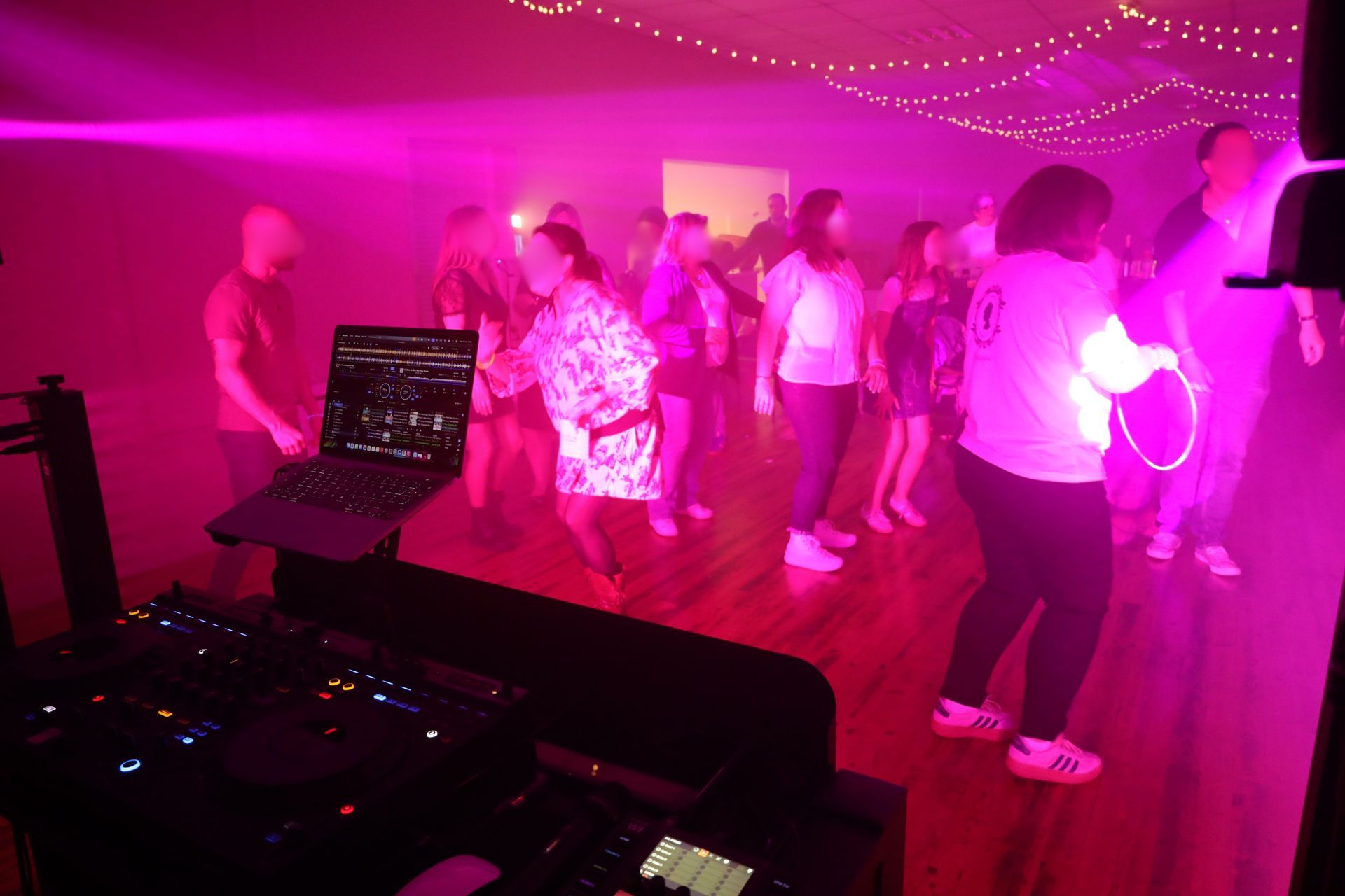 Des gens dansent dans une boîte de nuit éclairée en rose, à côté de la cabine du DJ.