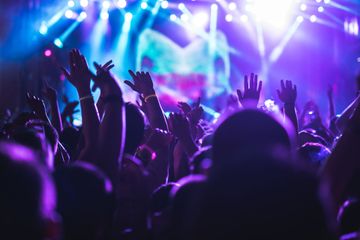 Foule les mains levées lors d'un concert sous des lumières de scène violettes et bleues