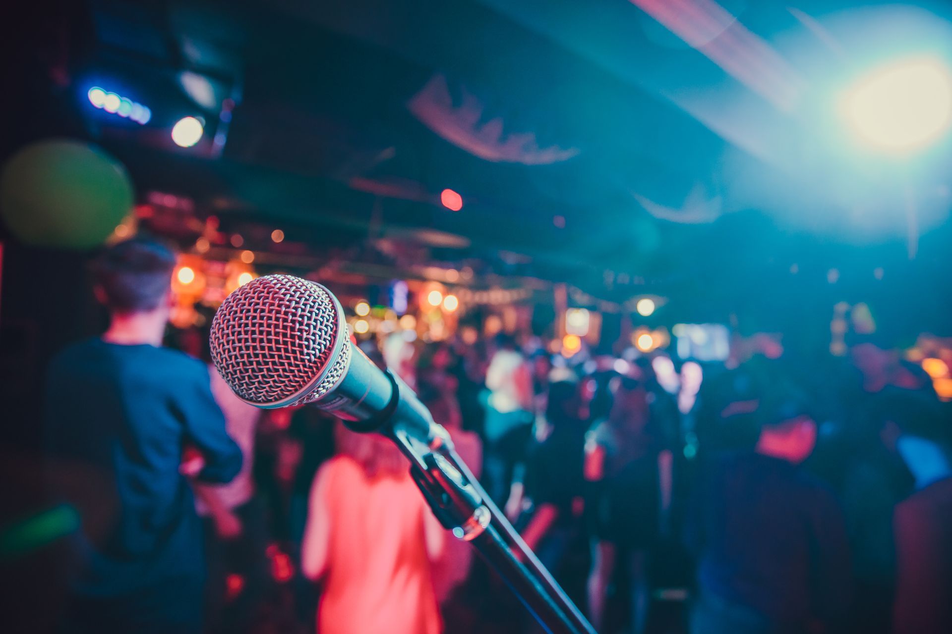 Microphone sur scène face à une foule floue dans une salle de concert sombre et colorée