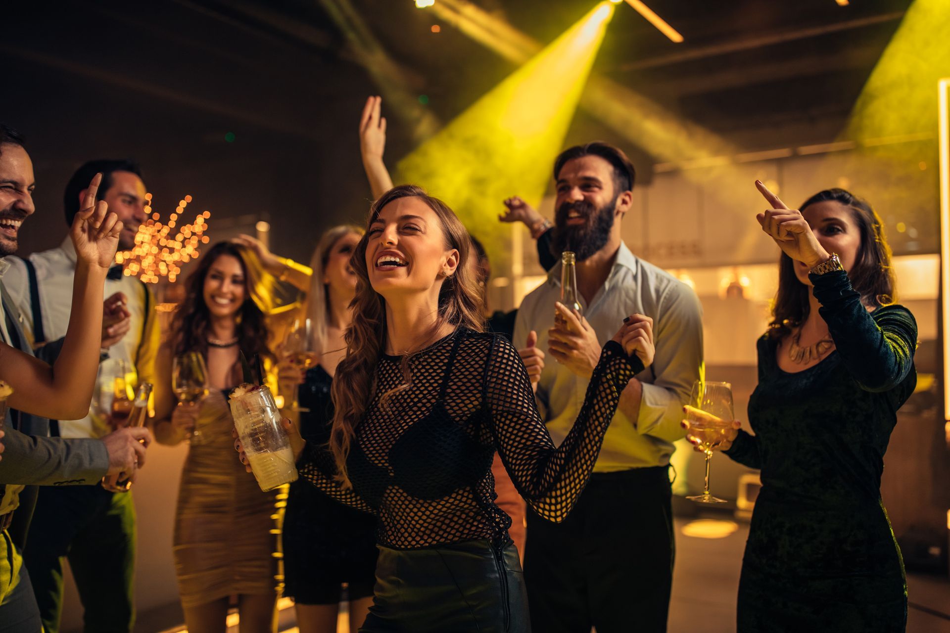 Des gens dansent et sourient sous une douce lumière jaune lors d'une fête animée en intérieur.