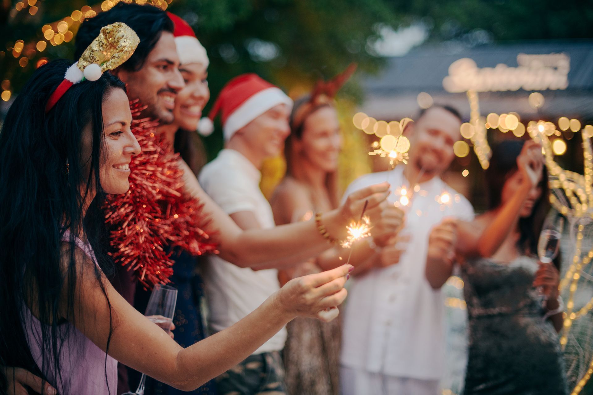 Des personnes tenant des cierges magiques et portant des chapeaux festifs lors d'un rassemblement de Noël en plein air au crépuscule