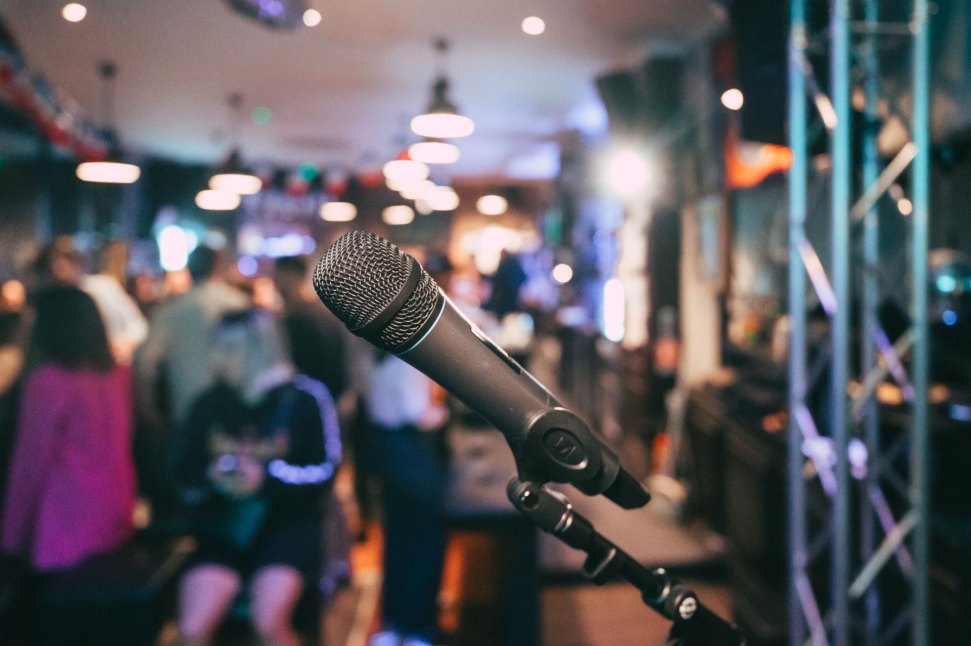 Microphone sur pied dans une salle de concert floue, avec des lumières de scène et une foule en arrière-plan.