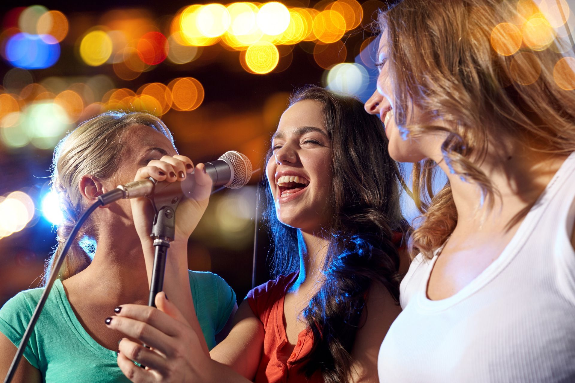 Trois femmes chantent dans des microphones lors d'un concert nocturne animé aux lumières colorées.