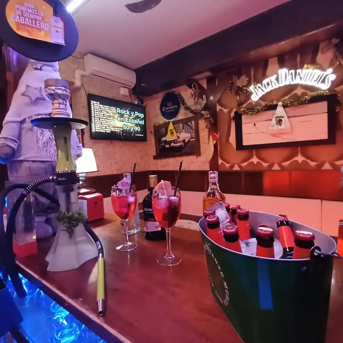 Interior del bar: cachimba, bebidas, botellas en cubo de hielo, TV, cartel de Jack Daniel's.