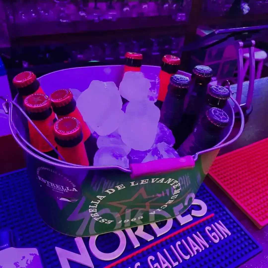 Cubo de botellas de cerveza en hielo sobre una barra, iluminado con luz violeta.