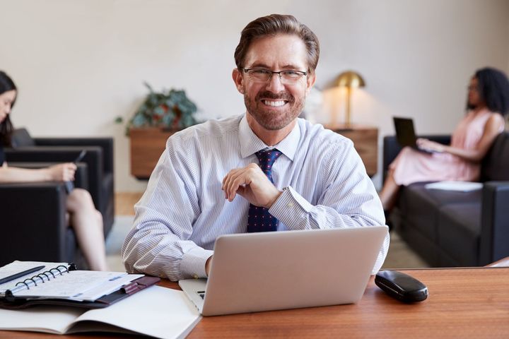 Mann mit Laptop und Notizbuch lächelt