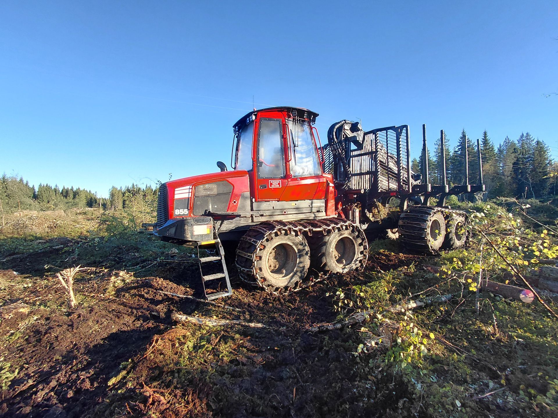Punainen metsäkone kiskoilla aukiolla, sininen taivas yläpuolella.