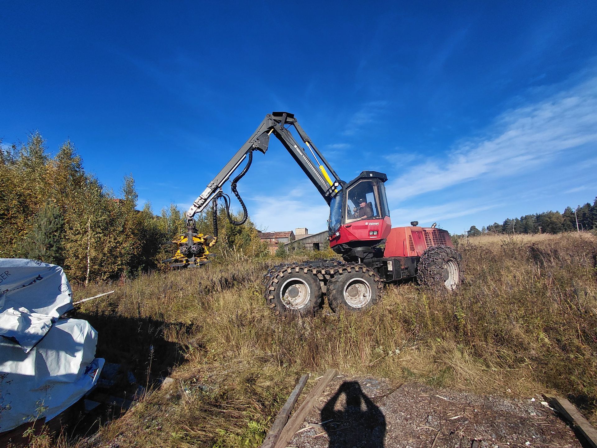 Punainen metsäkone raivaa pensasta pellolla sinisen taivaan alla.