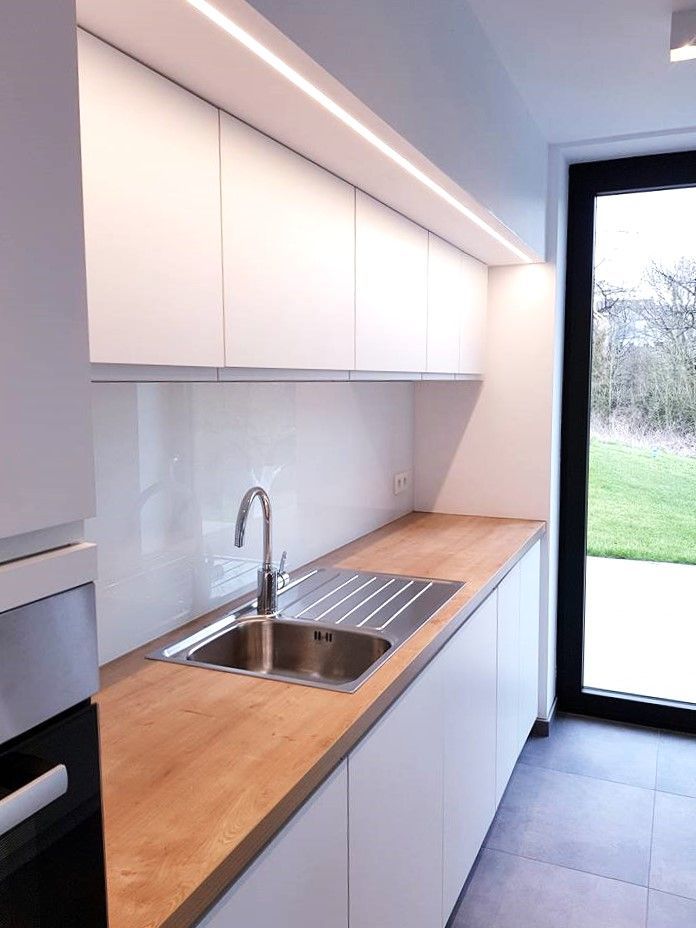 Cuisine blanche moderne avec comptoir en bois, évier en acier inoxydable et éclairage au plafond.