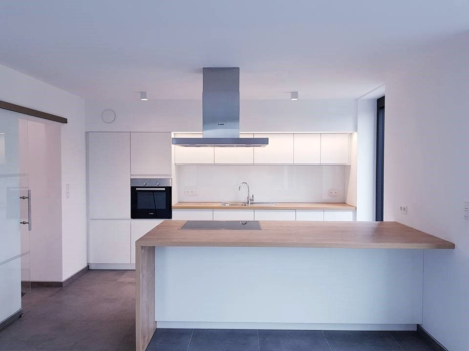 Cuisine blanche moderne avec îlot de comptoir en bois et hotte en acier inoxydable.