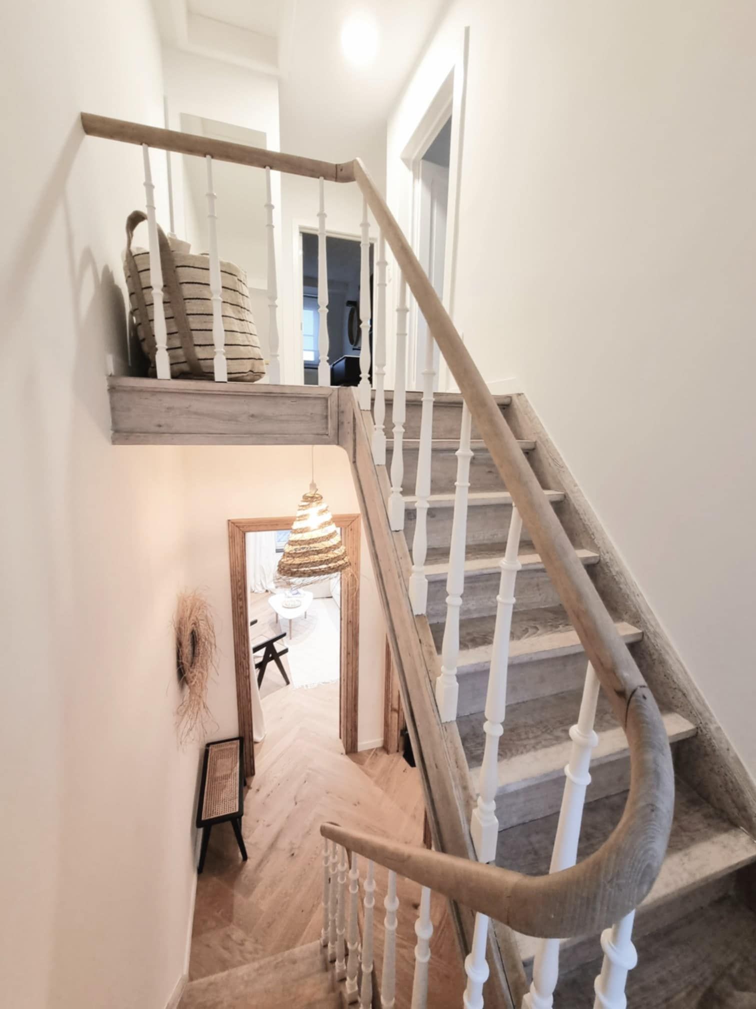 Escalier en bois avec balustres blancs et rampe courbée, menant à une pièce avec parquet.