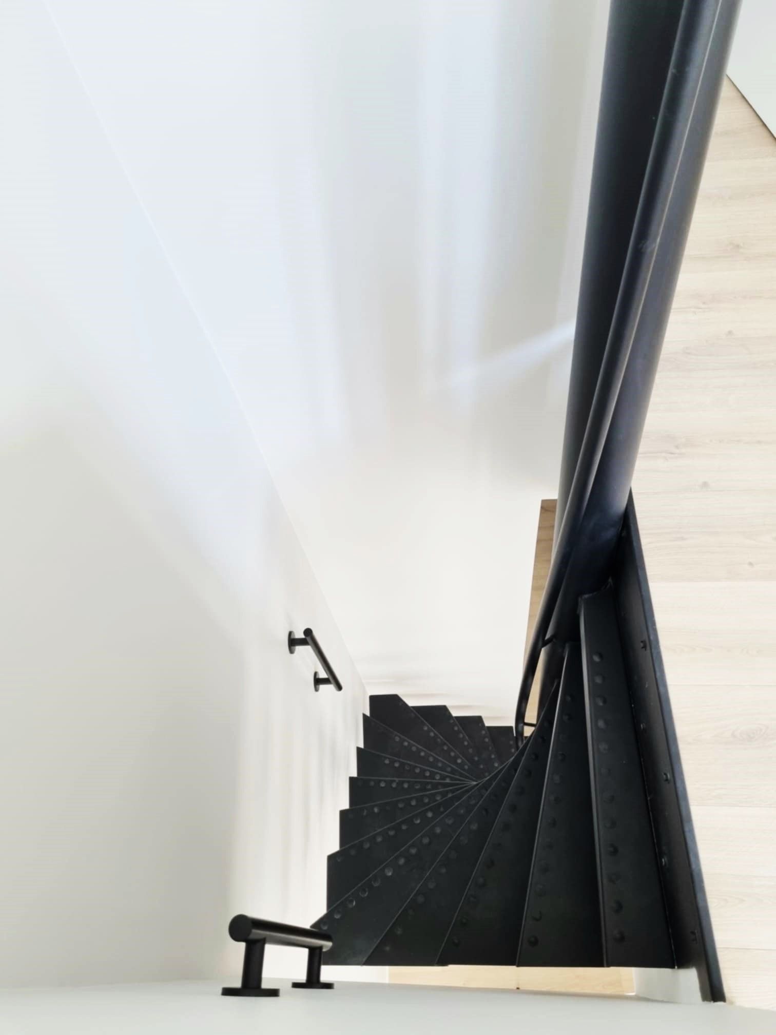 Vue aérienne d'un escalier en colimaçon noir avec une rampe noire contre un mur blanc.