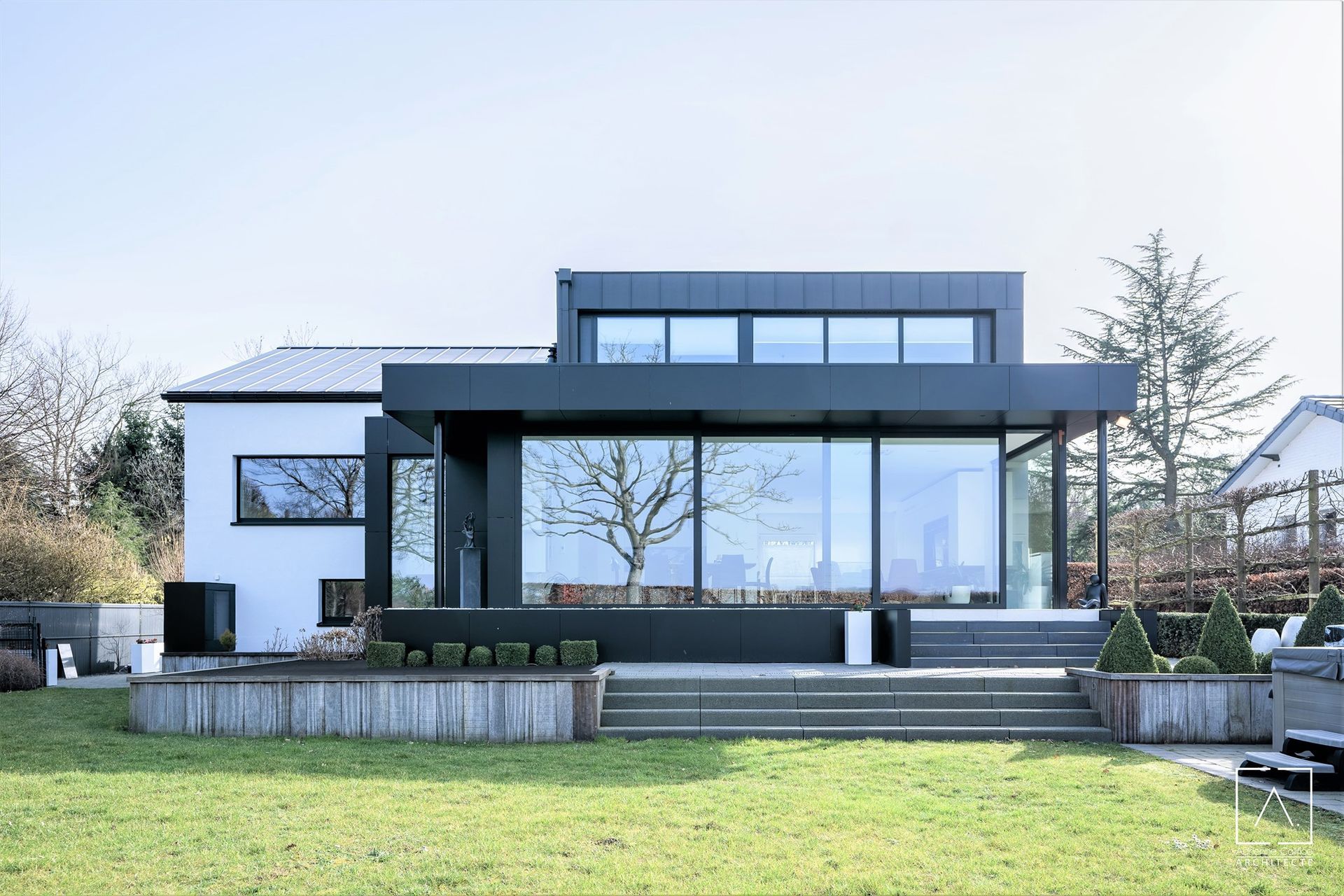 Maison blanche moderne avec des accents noirs et de grandes fenêtres en verre par une journée ensoleillée.