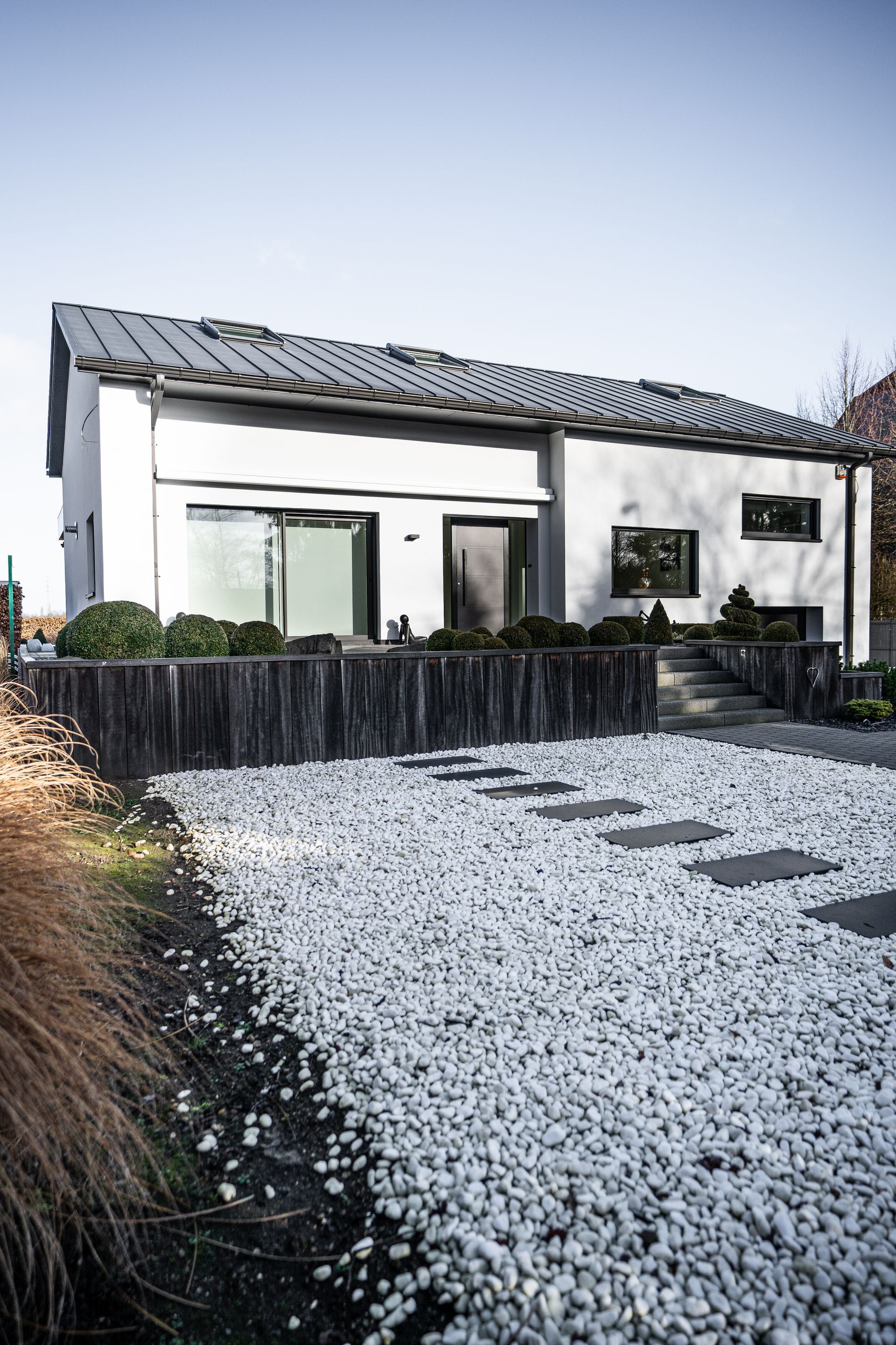 Maison blanche moderne avec garniture sombre, allée en gravier et clôture en bois.