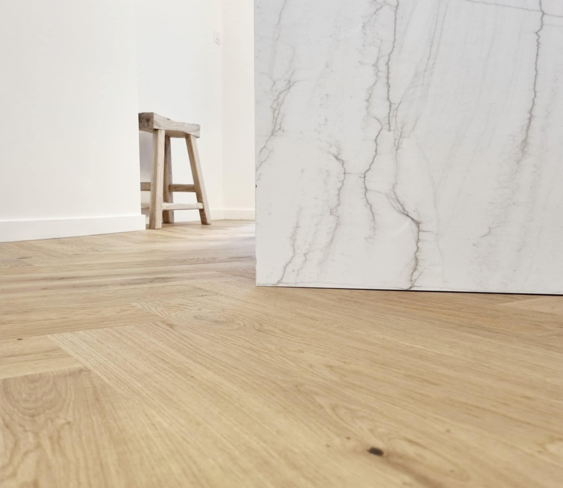 Plancher en bois clair, mur en marbre blanc et tabouret en bois dans une pièce.