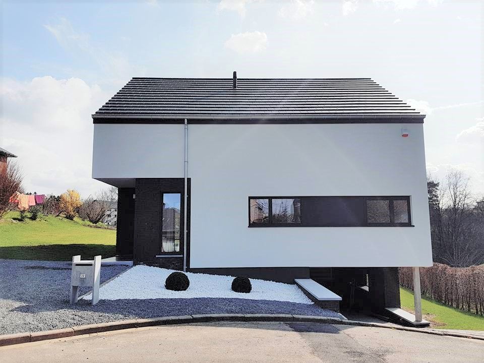 Maison moderne, blanche avec des accents noirs; située sur une légère pente.