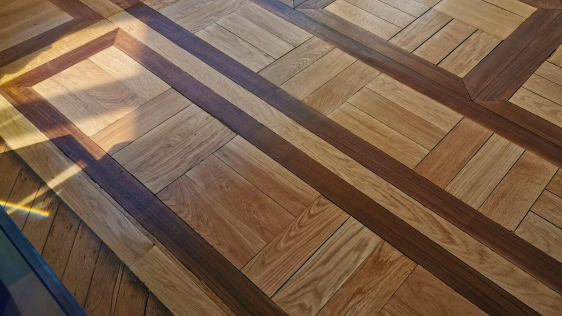 Vue en plongée d'un parquet à motifs, composé de carrés de chêne clair encadrés de larges bordures en bois brun foncé.