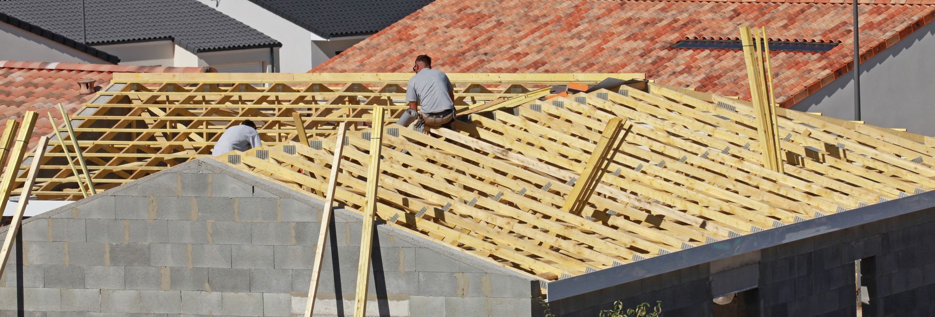 Deux ouvriers installent des fermes de toit en bois sur un immeuble résidentiel en construction.