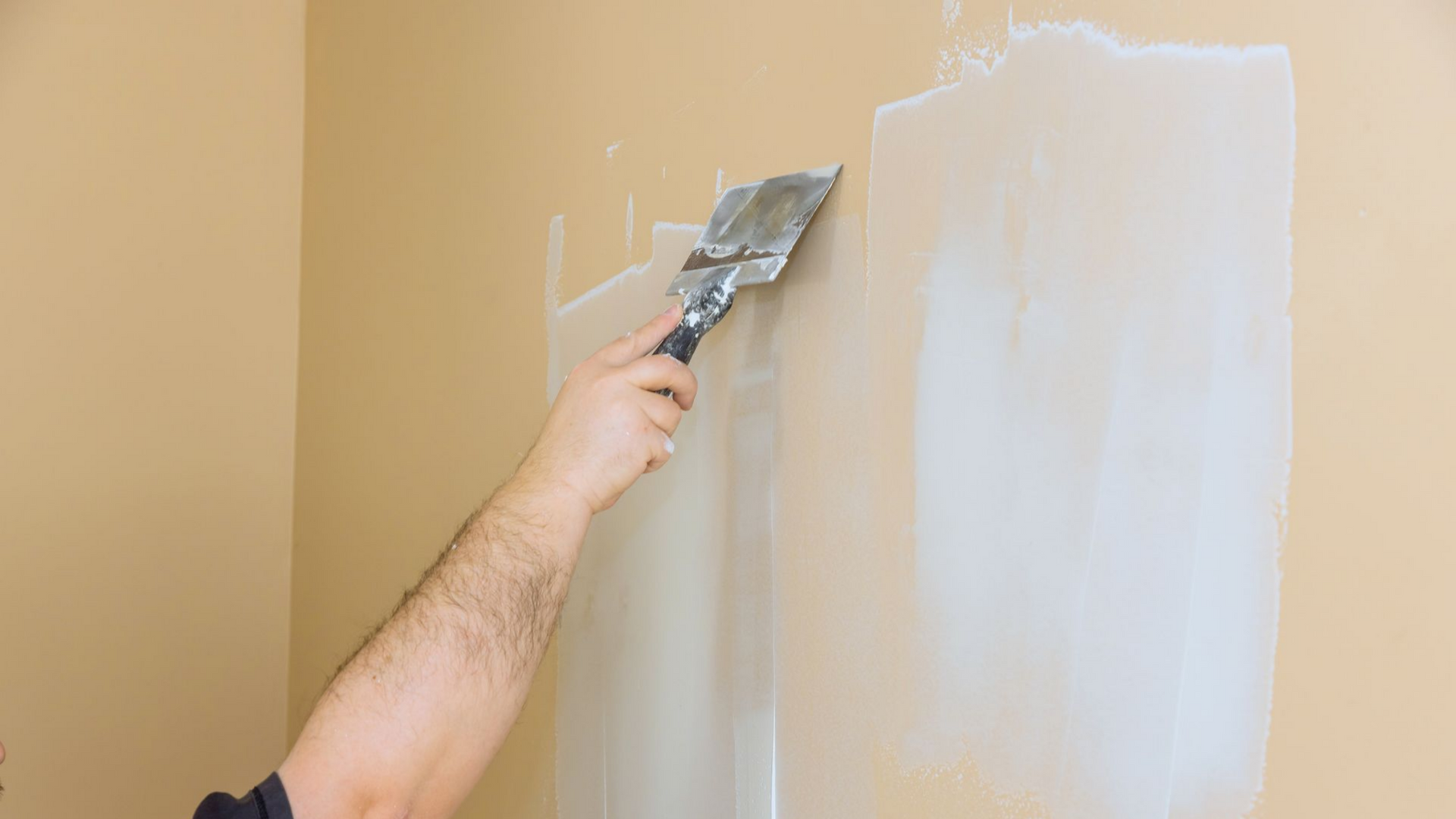 Main qui tient une spatule pour reboucher des trous sur un mur