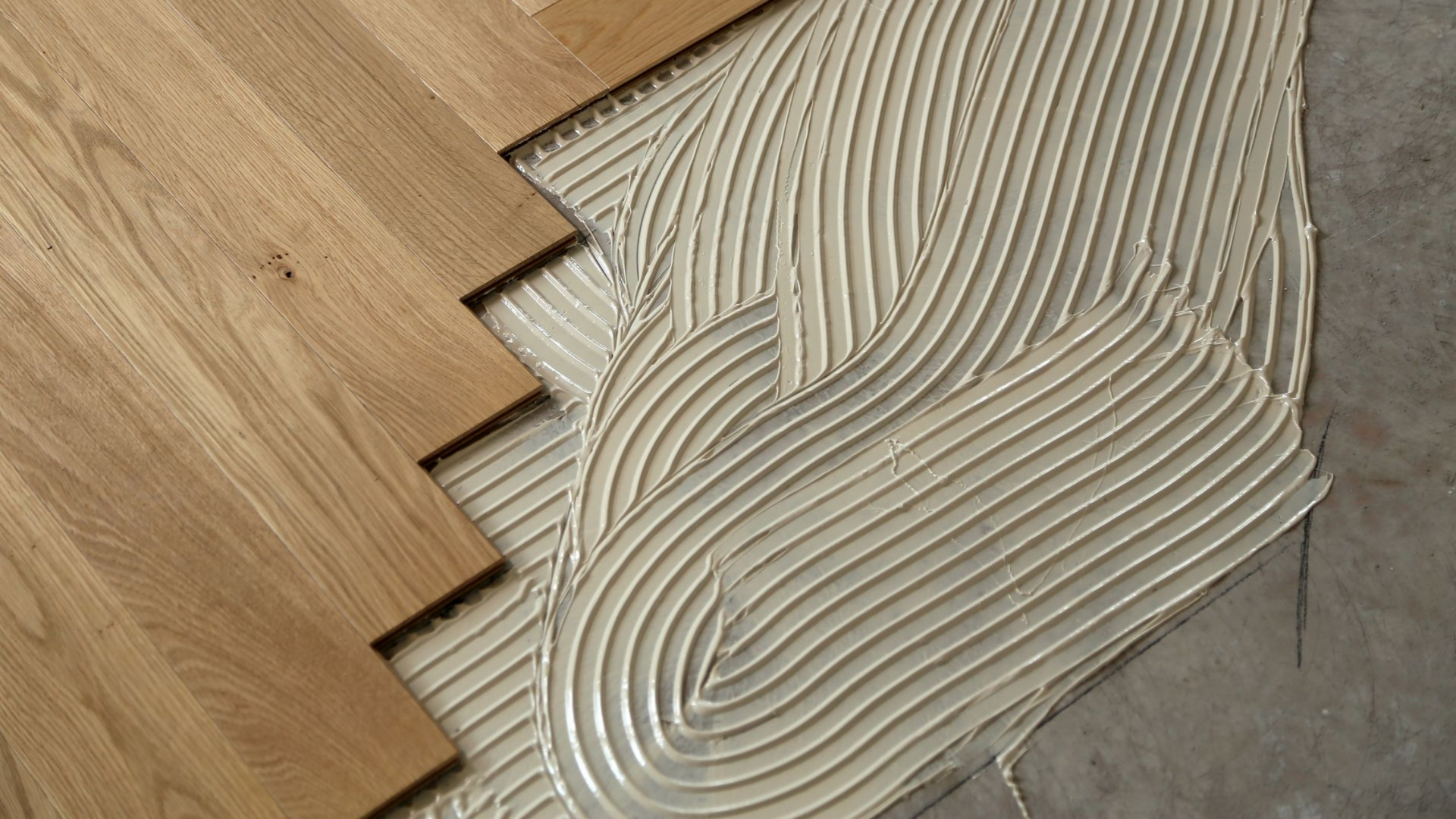 Un ouvrier portant des gants texturés utilise une ponceuse sur un parquet dans une pièce baignée de soleil.