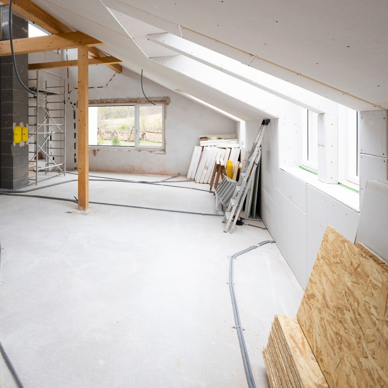 Rénovation de combles, avec des murs en plaques de plâtre non finies, des plafonds inclinés avec un puits de lumière.