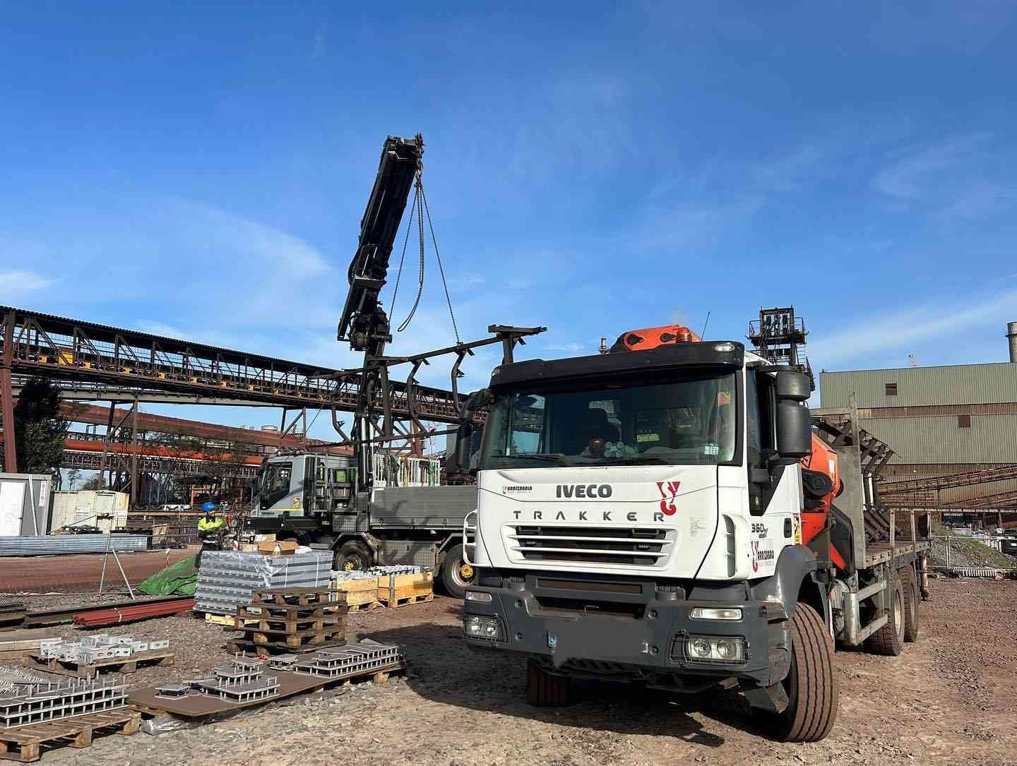 Camión volquete IVECO blanco en una obra de construcción industrial con grúa y estructuras de acero.