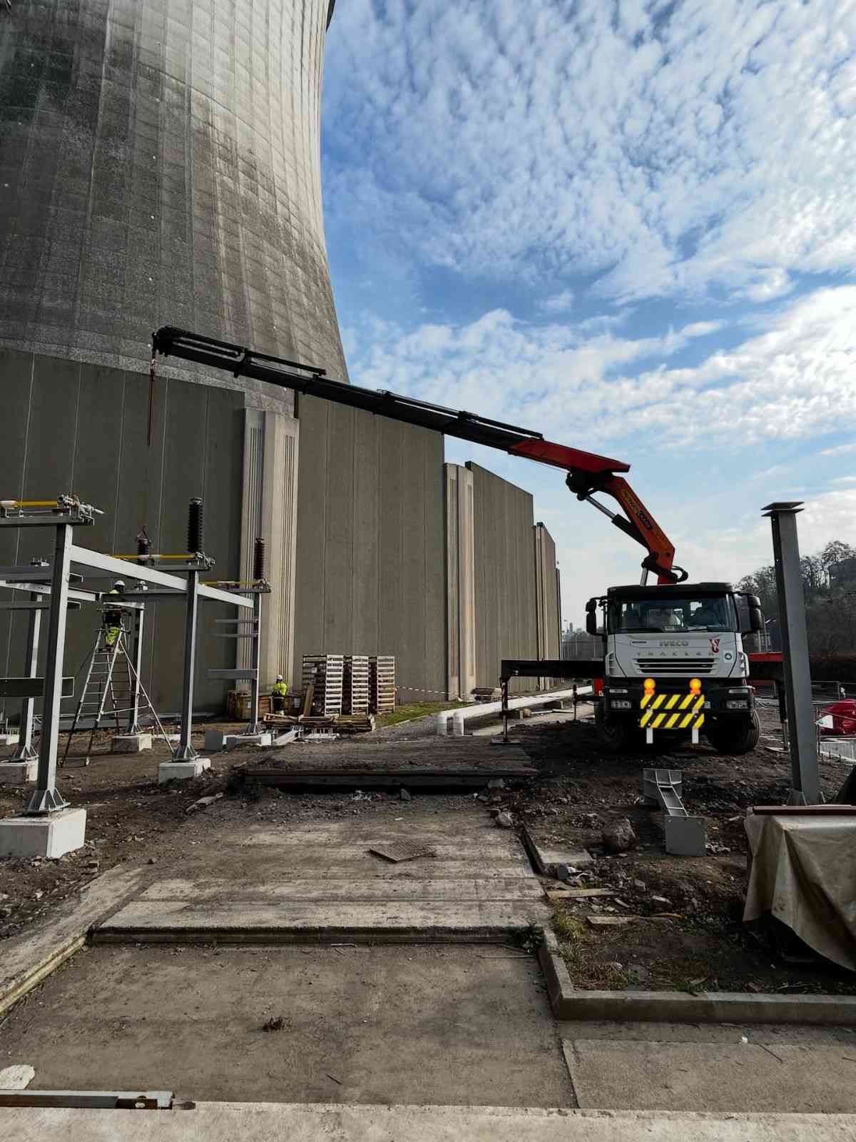 Zona industrial con una grúa roja junto a una gran torre de refrigeración de hormigón bajo un cielo nublado.