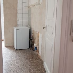 Ein kleiner Kühlschrank steht im Flur neben einer Tür.