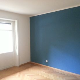 Ein leerer Raum mit einer blauen Wand und einem Fenster.