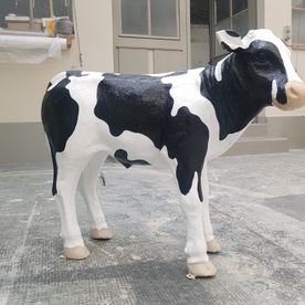 Eine schwarz-weiße Kuhstatue steht auf einem Gehweg vor einem Gebäude.