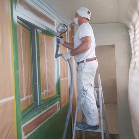 Ein Mann steht auf einer Leiter und streicht eine Wand.