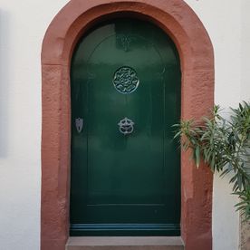 Eine grüne Tür mit einem roten Bogen auf einer weißen Wand.