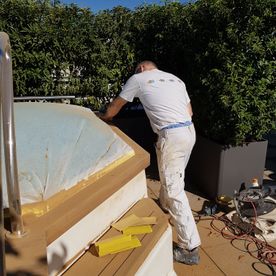 Ein Mann in weißen Hosen arbeitet an einem Whirlpool auf einer Terrasse.