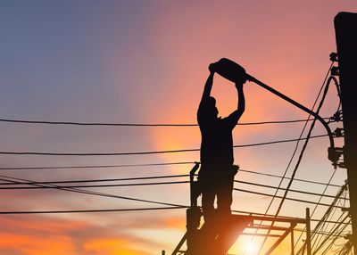 Zwei Energiearbeiter reparieren in Hubarbeitsbühnen Stromleitungen neben einem Strommast unter blauem Himmel.