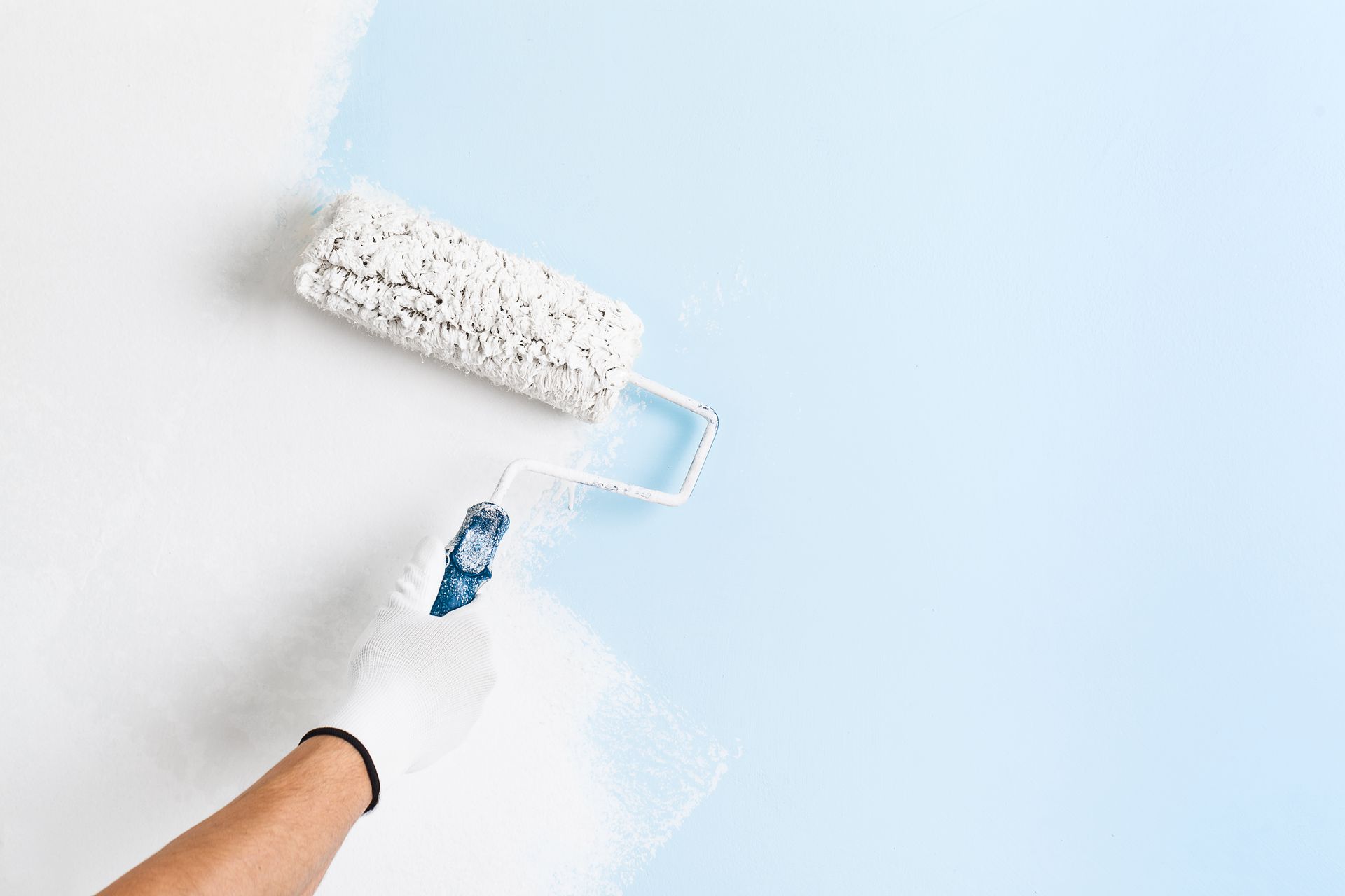 Une main tenant un rouleau de peinture et peignant en blanc un mur bleu d'une maison