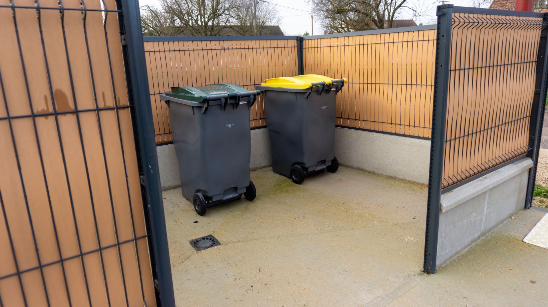Un local poubelle disposant d'une poubelle avec un couvercle jaune et une autre avec un couvercle vert