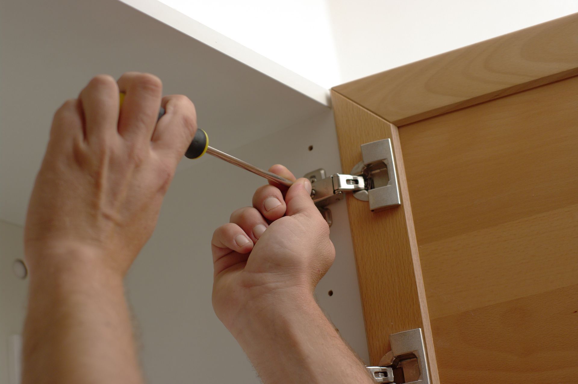Un ouvrier fixe la vis de la charnière d'une porte en bois.