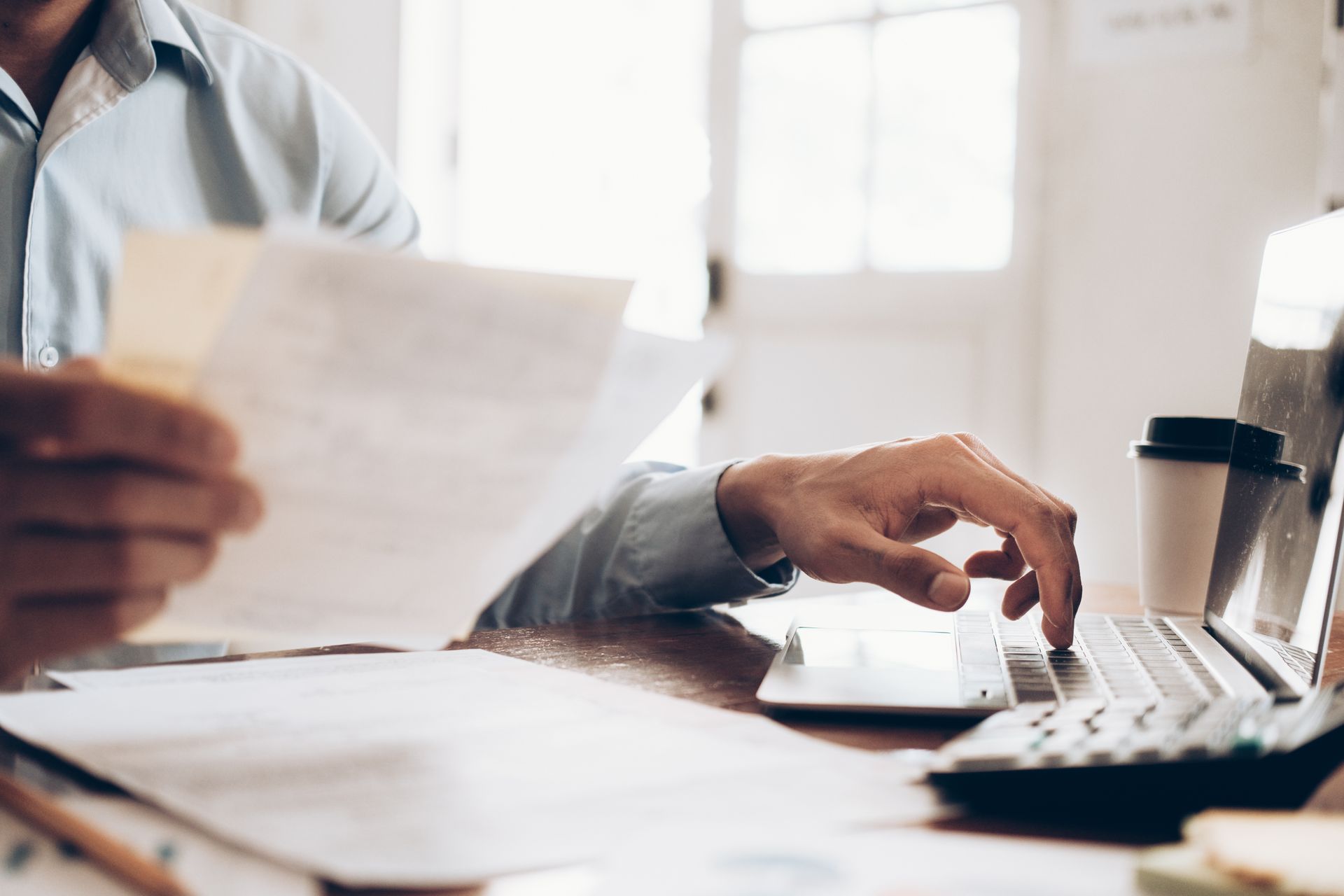 Personne en train de taper sur un clavier en tenant une feuille dans sa main