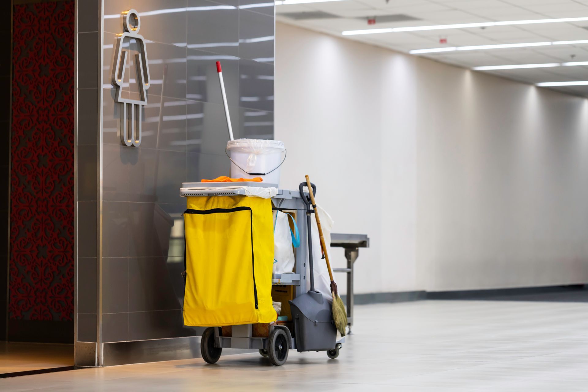 Chariot de nettoyage avec seau à serpillière jaune dans un couloir moderne.