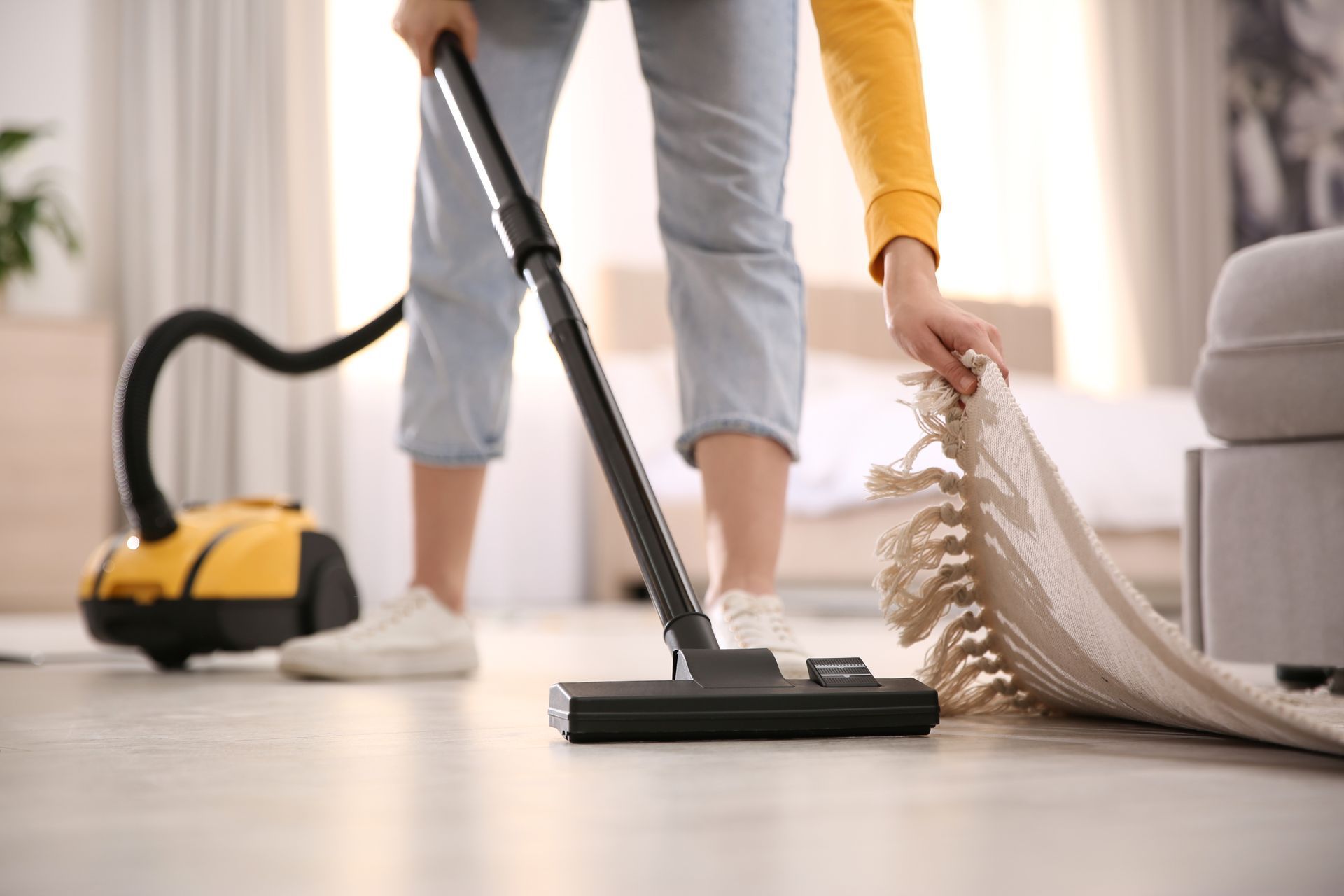 Une personne passe l'aspirateur dans un salon à côté d'un tapis enroulé et d'outils de nettoyage.