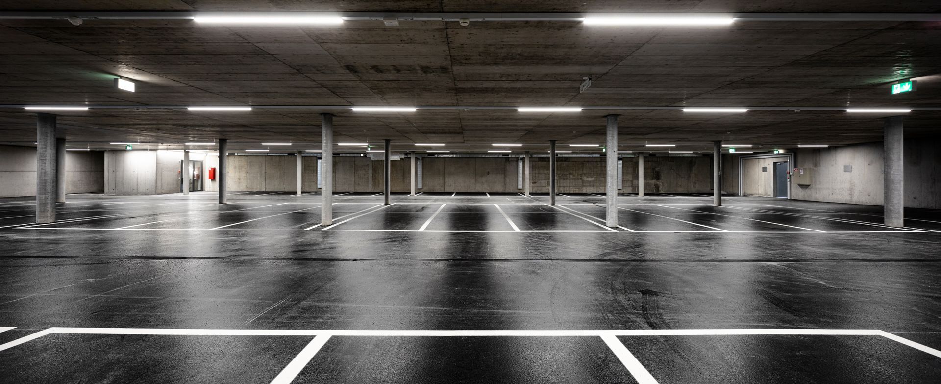 Parking intérieur vide, sol mouillé et lignes de stationnement blanches.