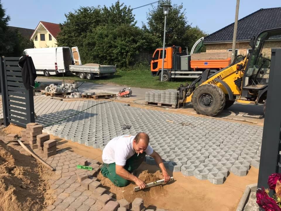 Ein Mann kniet auf dem Boden und arbeitet an einer Einfahrt.