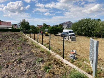 Ein Zaun umgibt ein Feld mit einem im Hintergrund geparkten weißen Lieferwagen.