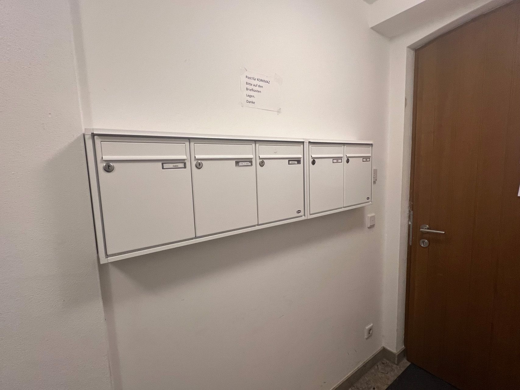 Eine Reihe weißer Briefkästen an einer Wand neben einer Tür.