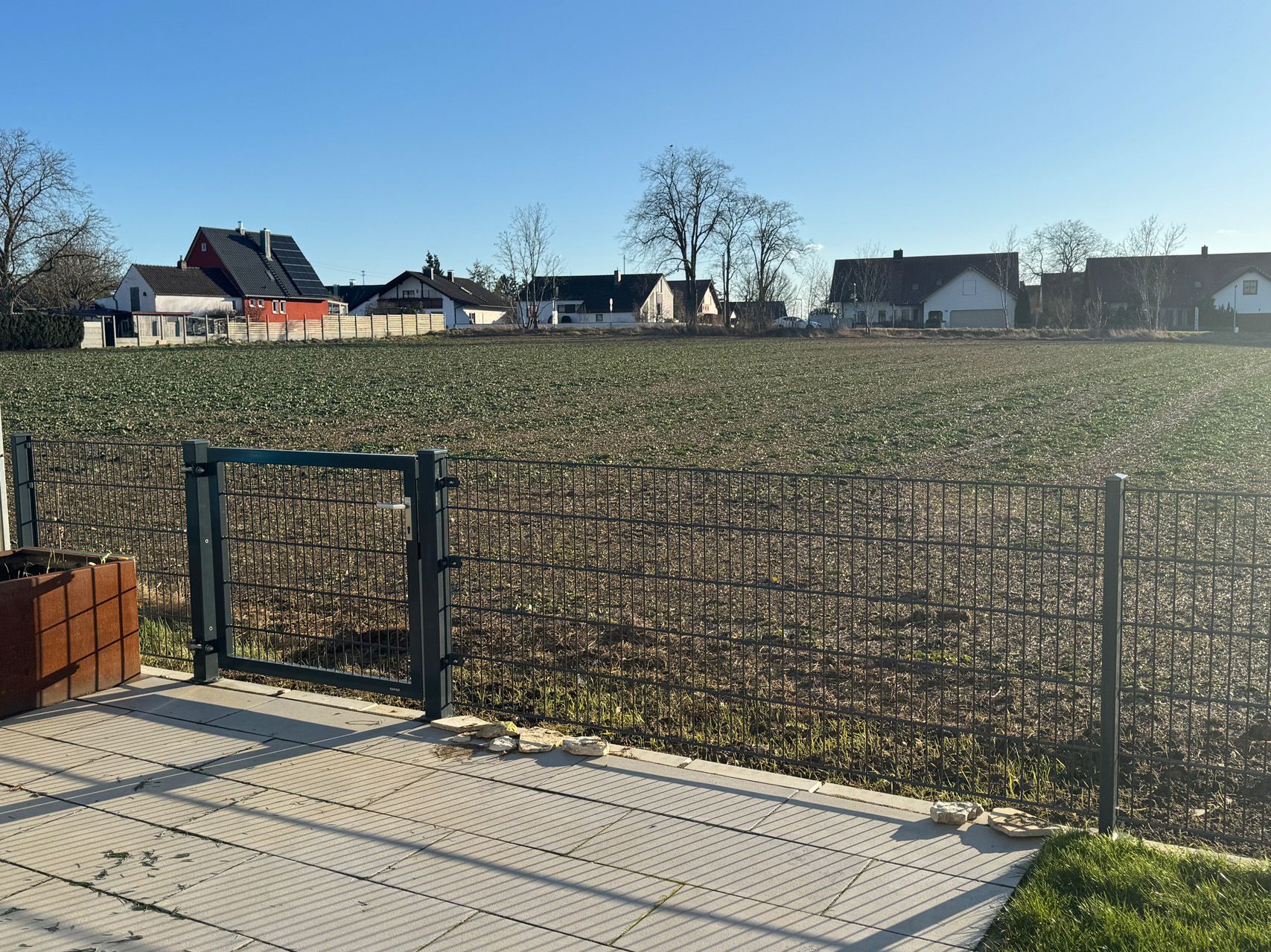 Ein Zaun umgibt ein Feld mit Häusern im Hintergrund.