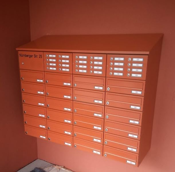 Eine Reihe orangefarbener Briefkästen an einer roten Wand