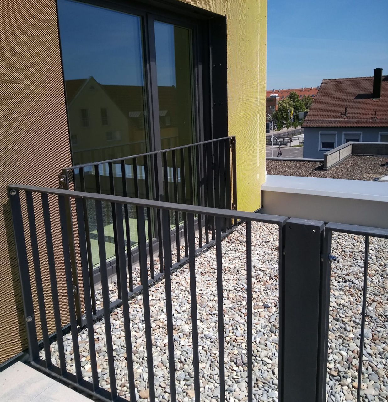 Ein Balkon mit einem schwarzen Geländer und einem gelben Gebäude im Hintergrund