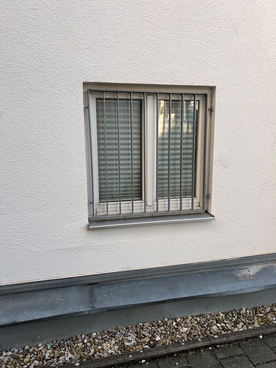An der Seite eines Gebäudes befindet sich ein vergittertes Fenster.